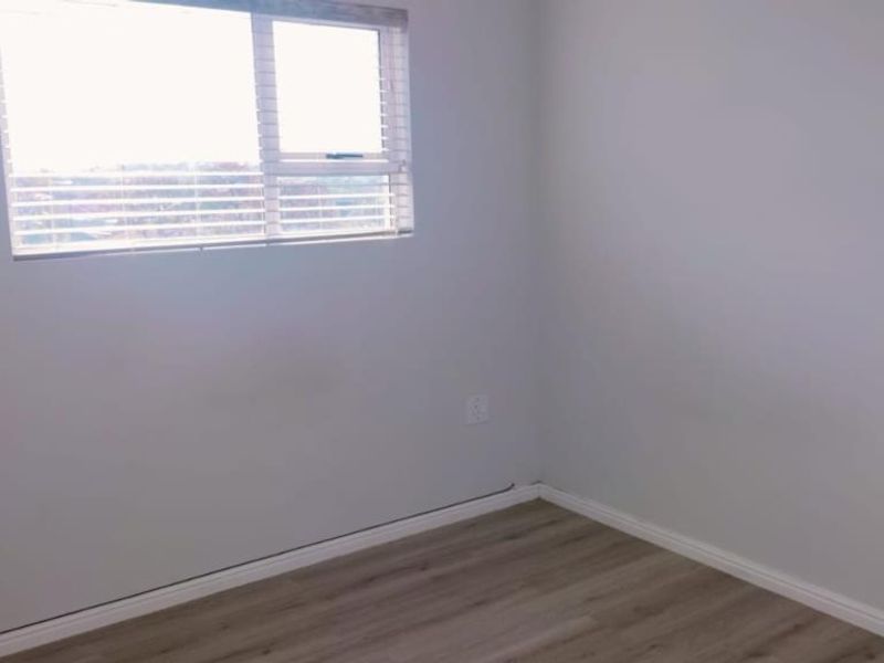 A clean, empty bedroom featuring modern laminate flooring, neutral walls, and a window fitted with blinds.