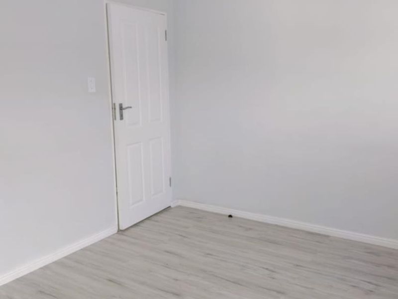 A clean, empty bedroom featuring light-toned laminate flooring and neutral wall finishes, providing a versatile blank canvas for interior design.