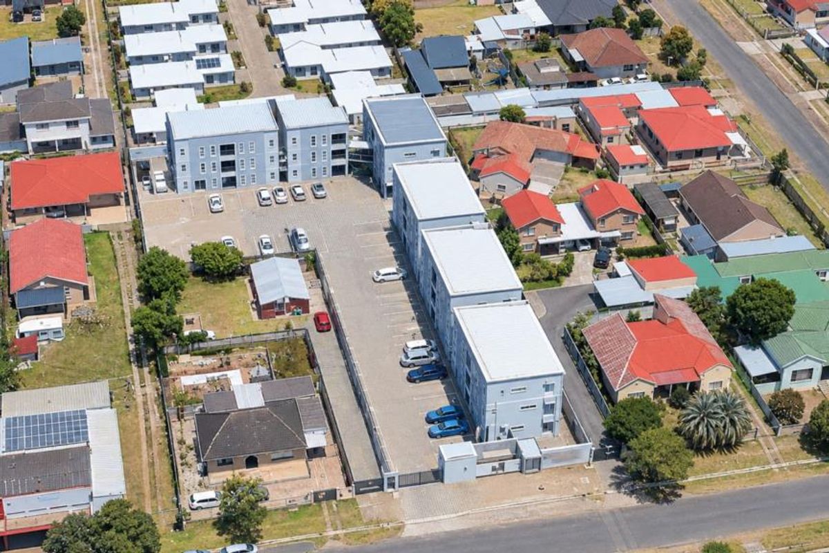 Aerial view of a residential apartment complex featuring multiple buildings, a paved parking lot, and secure perimeter fencing within a suburban neighborhood.