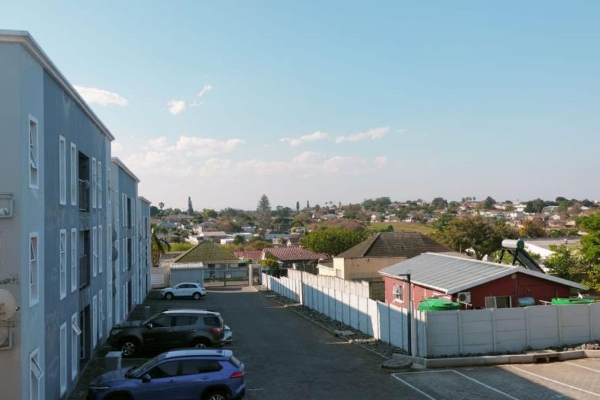 An elevated view of the apartment complex rear exterior, featuring a paved parking area, precast boundary walling, and surrounding residential neighborhood views.