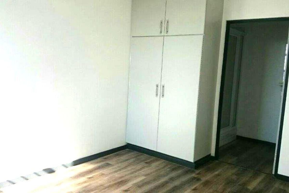 A clean, empty bedroom featuring modern laminate flooring and built-in cupboards, offering a neutral canvas for personalization.