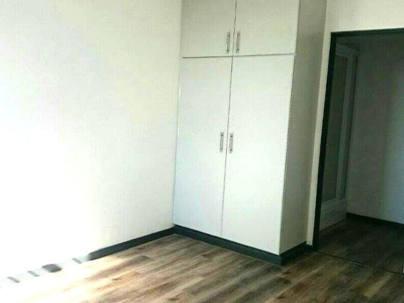 A clean, empty bedroom featuring modern laminate flooring and built-in cupboards, offering a neutral canvas for personalization.