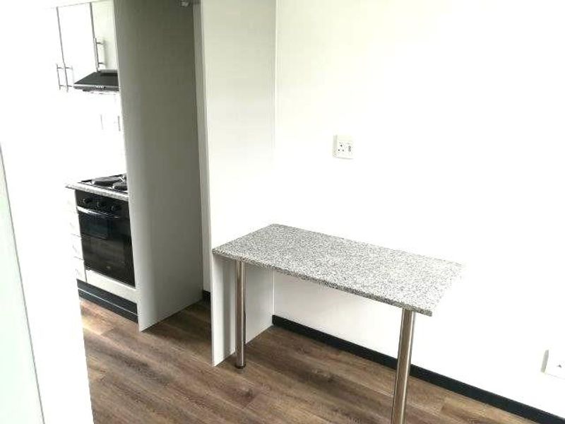 A clean, modern kitchen area featuring laminate flooring, built-in oven with gas hob, extractor fan, and a functional granite breakfast bar.