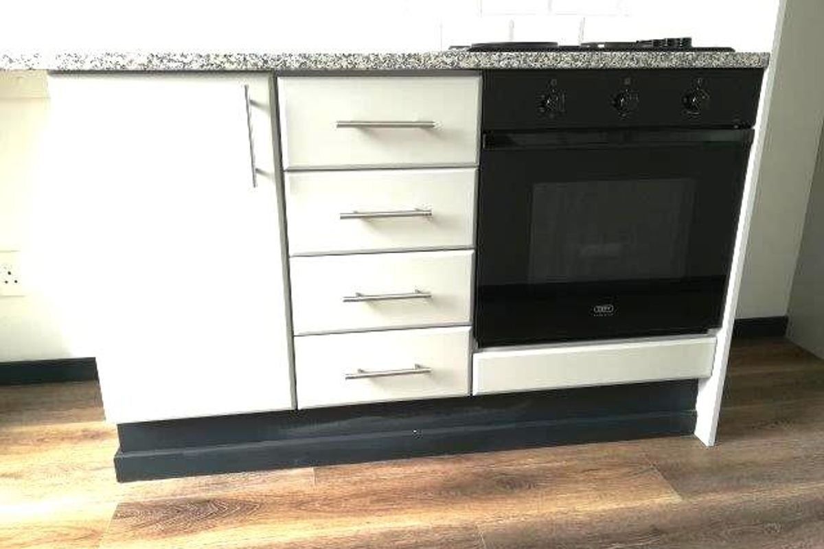 A modern kitchen section featuring a granite countertop, built-in oven, electric hob, and white cabinetry with a subway tile backsplash.