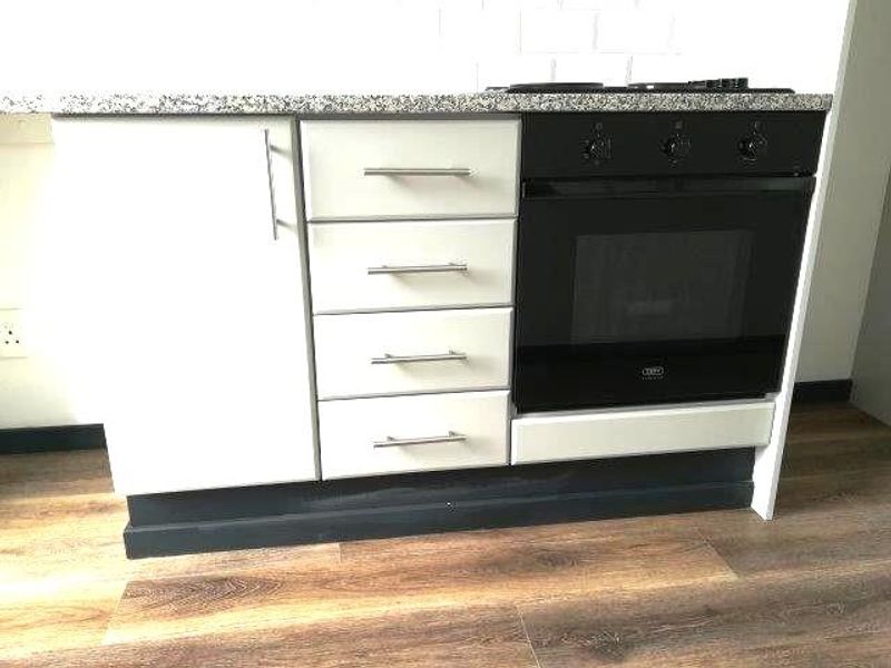 A modern kitchen section featuring a granite countertop, built-in oven, electric hob, and white cabinetry with a subway tile backsplash.