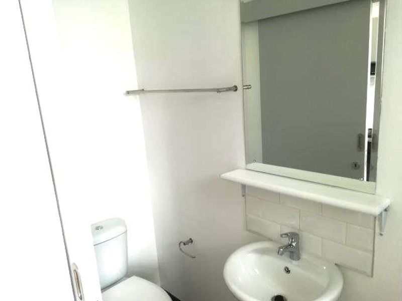 A compact bathroom featuring a pedestal basin with a tiled splashback, a wall-mounted mirror, and a standard toilet.
