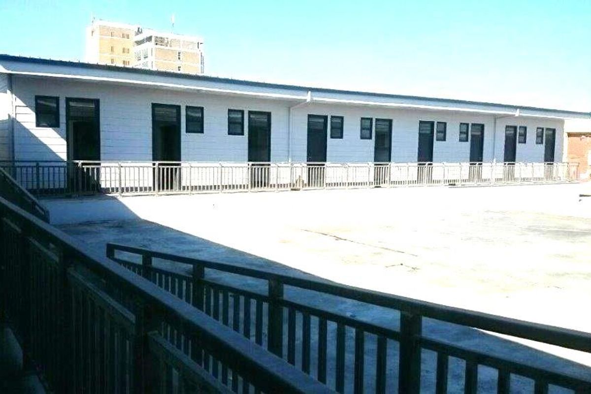 Exterior view of a multi-unit apartment building featuring a large concrete terrace, metal safety railings, and multiple individual unit access points.