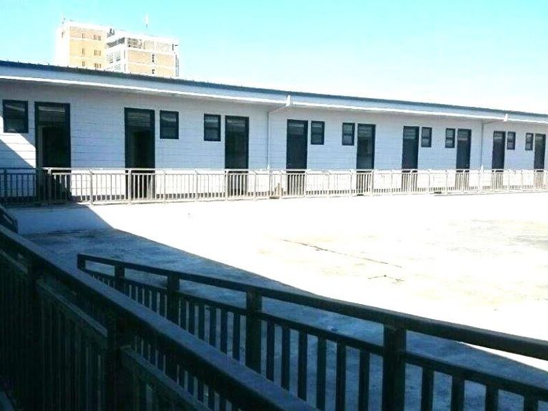 Exterior view of a multi-unit apartment building featuring a large concrete terrace, metal safety railings, and multiple individual unit access points.