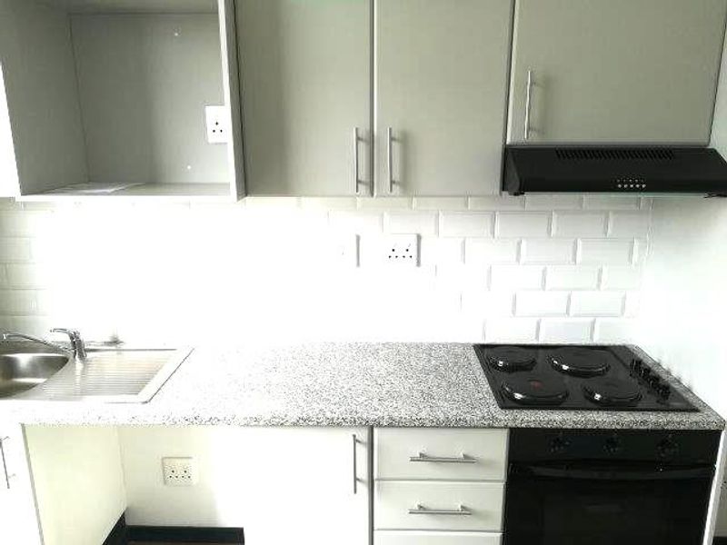 Modern kitchen featuring granite countertops, subway tile backsplash, built-in oven, electric hob, extractor fan, and ample cabinetry.