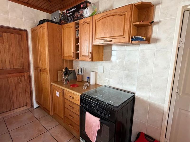 A functional kitchen featuring wooden cabinetry, tiled backsplash, and a freestanding stove, complemented by a timber ceiling and tiled flooring.