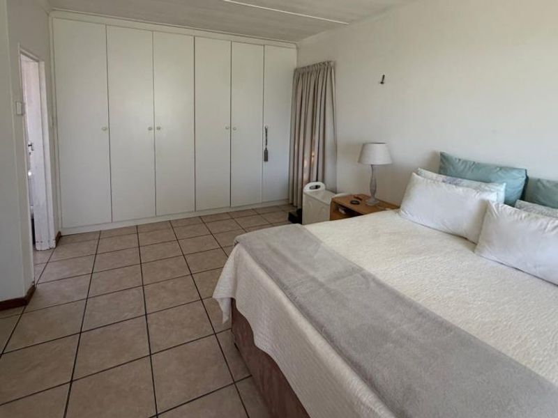 Spacious bedroom featuring extensive built-in cupboards and neutral tiled flooring, offering a clean and functional layout.