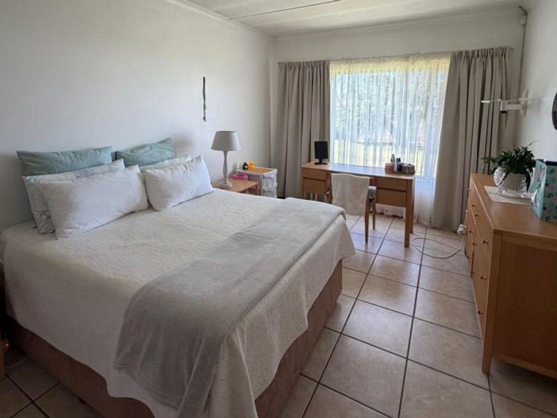 A spacious bedroom featuring tiled flooring and a large window with curtains, providing natural light and a functional layout.