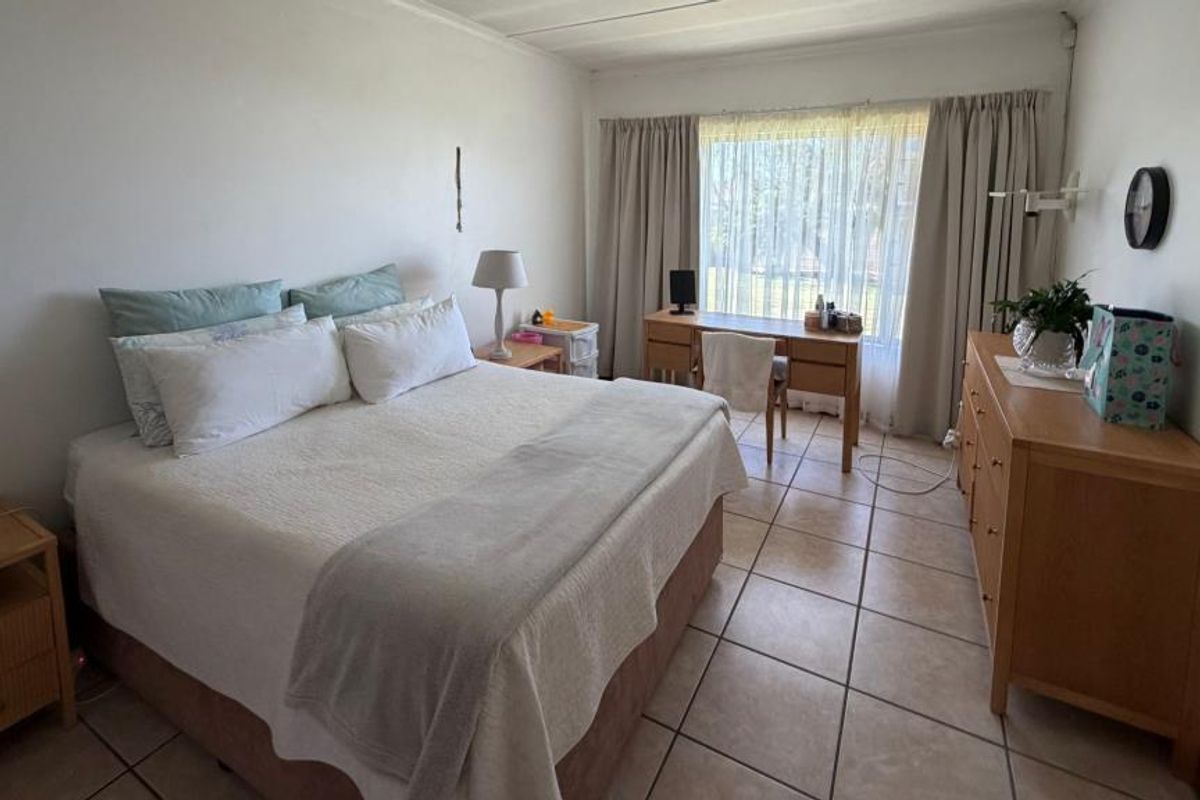 A spacious bedroom featuring tiled flooring and a large window with curtains, providing natural light and a functional layout.