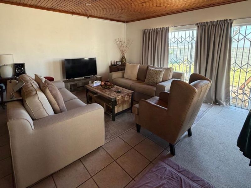 A living room featuring tiled flooring, a timber-paneled ceiling, and a sliding glass door with security gate providing access to the exterior.