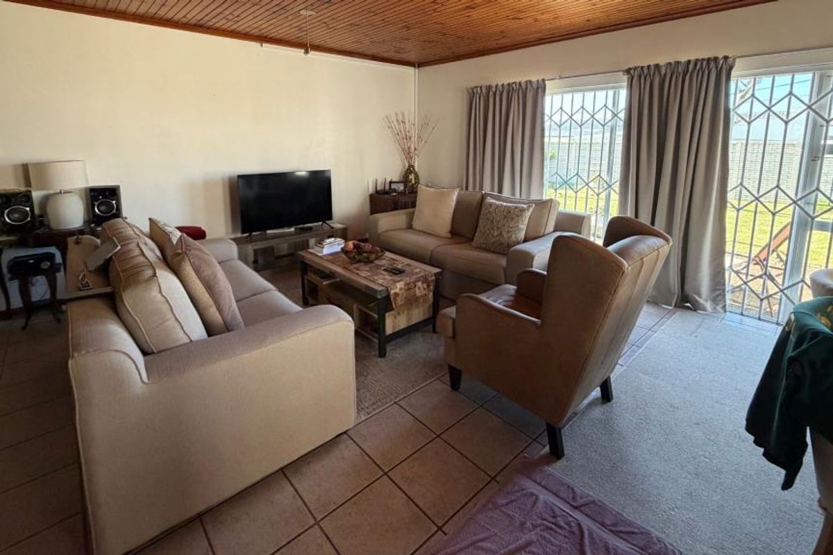 A living room featuring tiled flooring, a timber-paneled ceiling, and a sliding glass door with security gate providing access to the exterior.