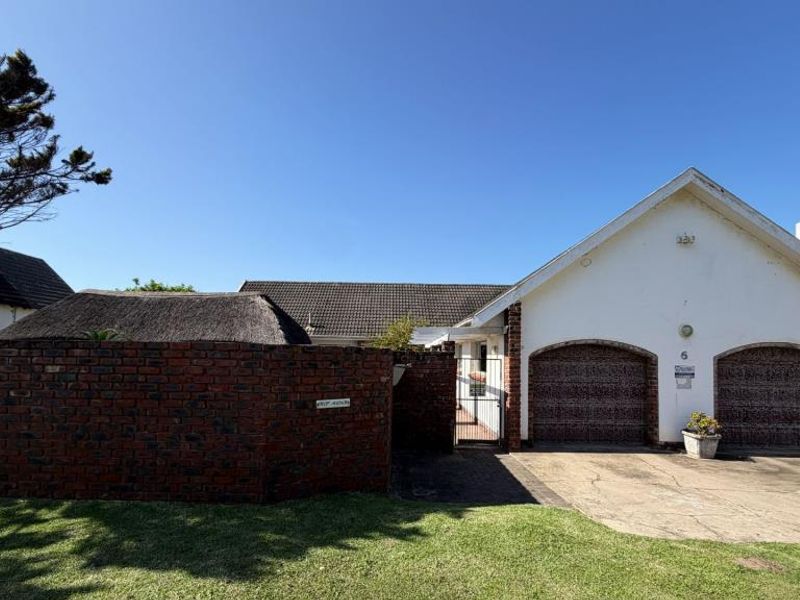 Front elevation of a residential property featuring a double garage, brick boundary wall, and paved driveway access.