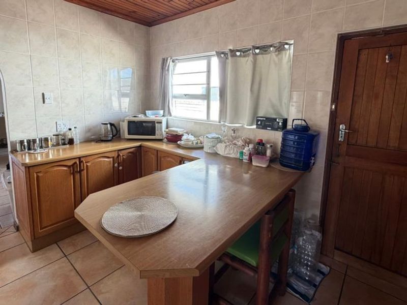 A functional kitchen featuring wooden cabinetry, a breakfast nook, tiled walls, and a wooden ceiling, offering a traditional layout with direct access to adjacent living areas.