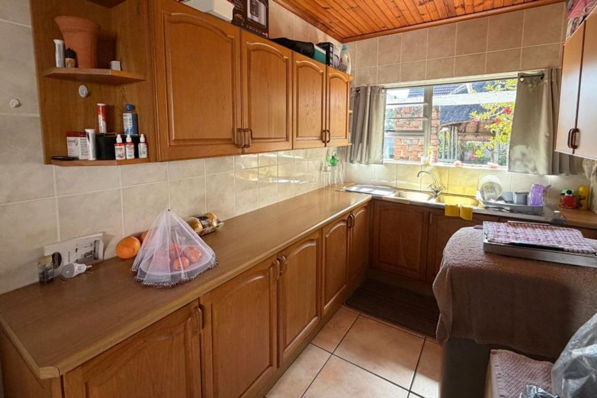 A functional kitchen featuring wooden cabinetry, laminate countertops, a stainless steel sink, and tiled finishes, offering a classic layout with potential for modern updates.