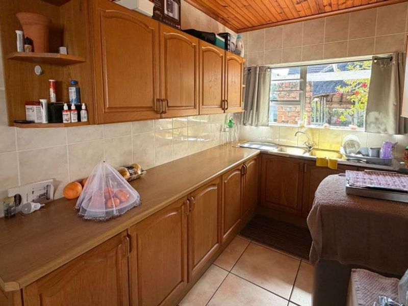 A functional kitchen featuring wooden cabinetry, laminate countertops, a stainless steel sink, and tiled finishes, offering a classic layout with potential for modern updates.