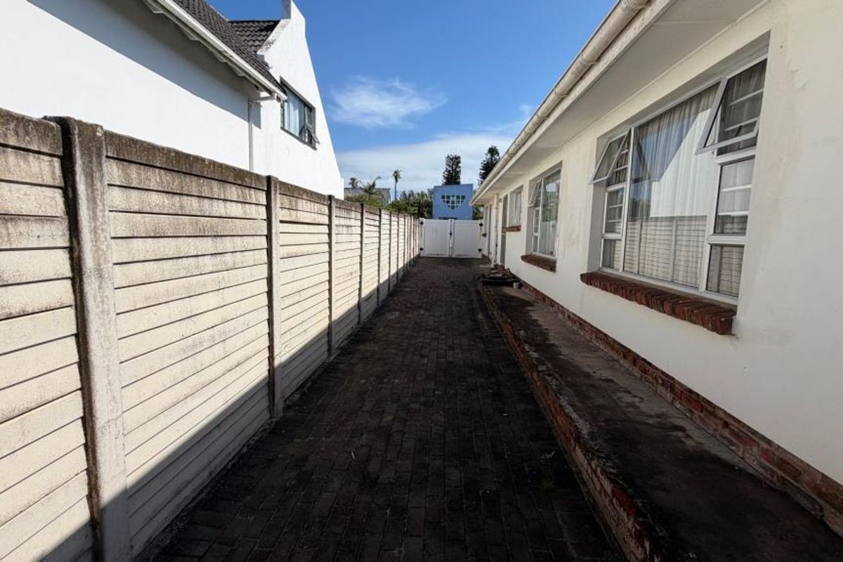 A narrow side passage featuring a precast concrete boundary wall, brick paving, and exterior access to the main dwelling structure.