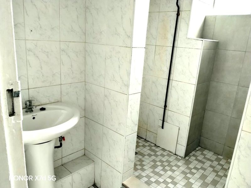 A functional bathroom featuring a pedestal basin and a separate shower area with tiled finishes throughout.