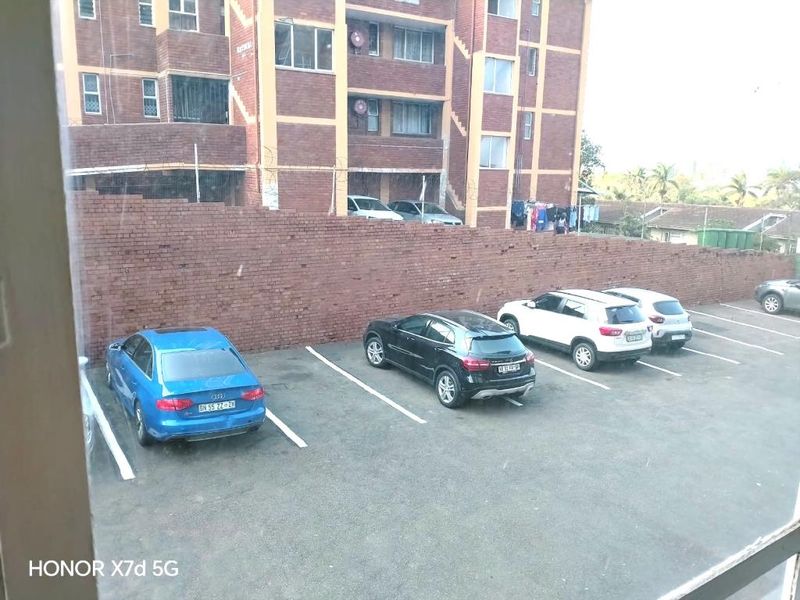 View of the apartment complex rear parking area featuring a brick boundary wall and paved parking bays.