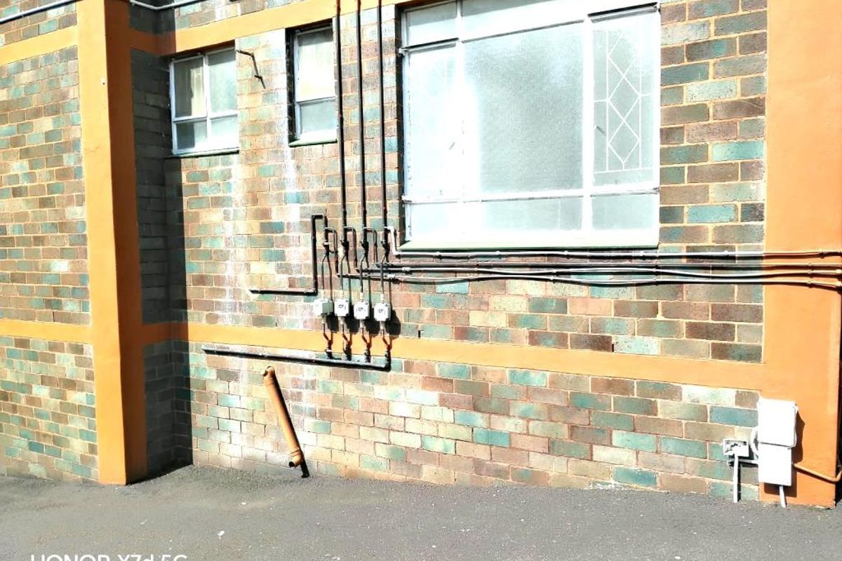 Exterior rear view of an apartment building featuring brick facade, exposed utility conduits, and multiple electrical meters.