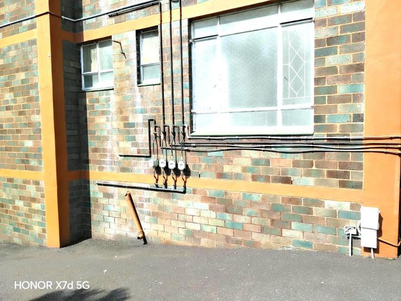 Exterior rear view of an apartment building featuring brick facade, exposed utility conduits, and multiple electrical meters.