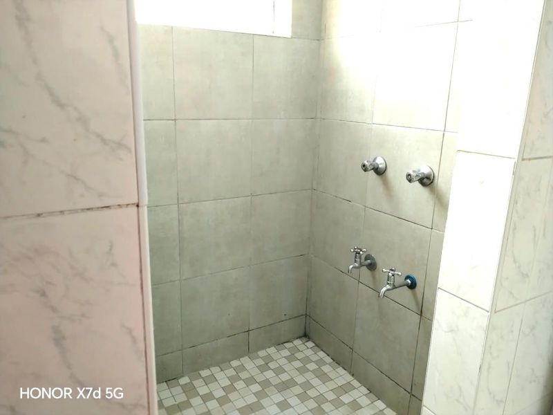 A basic shower enclosure featuring tiled walls and flooring with standard plumbing fixtures, requiring cosmetic updates to improve its overall condition.