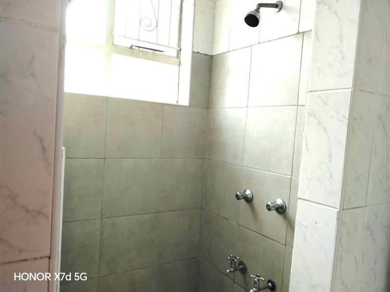 A functional shower area featuring tiled walls, a standard shower head, and mixer taps, requiring cosmetic updates to improve its overall condition.