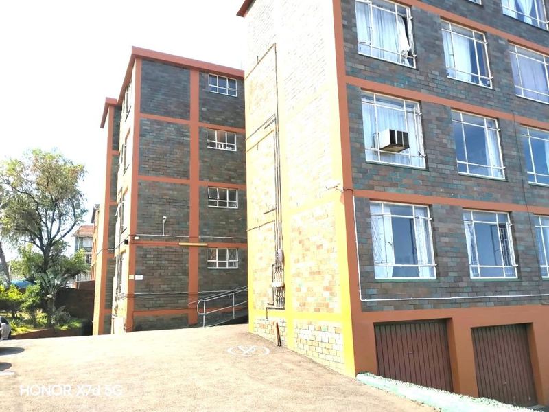 Exterior view of a multi-story apartment building featuring brick facade, paved driveway, and ground-level garage access.
