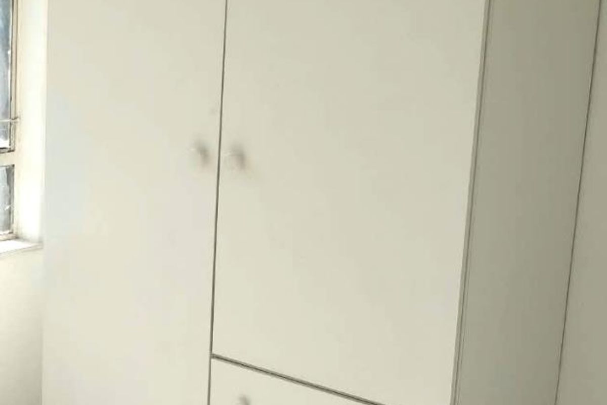 A bedroom featuring a white built-in wardrobe with integrated drawers and tiled flooring.
