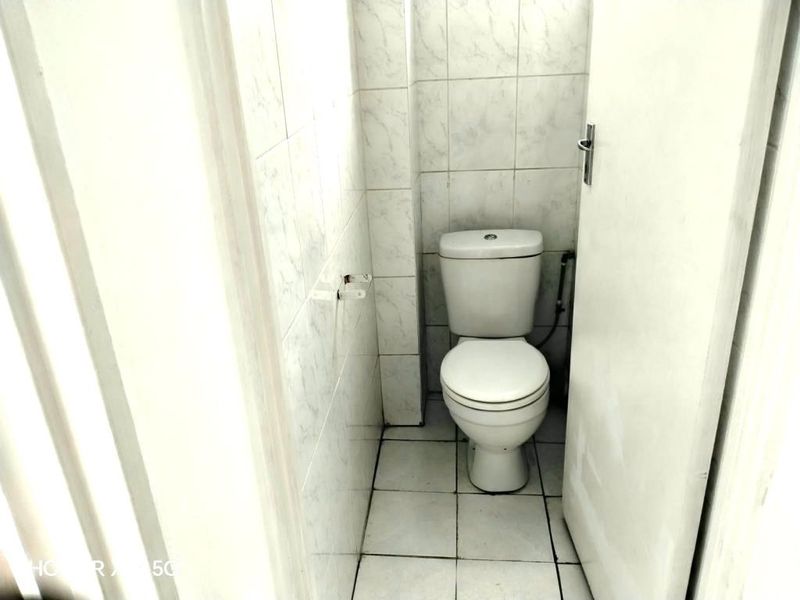 A compact bathroom featuring a standard toilet, finished with white ceramic wall and floor tiles.