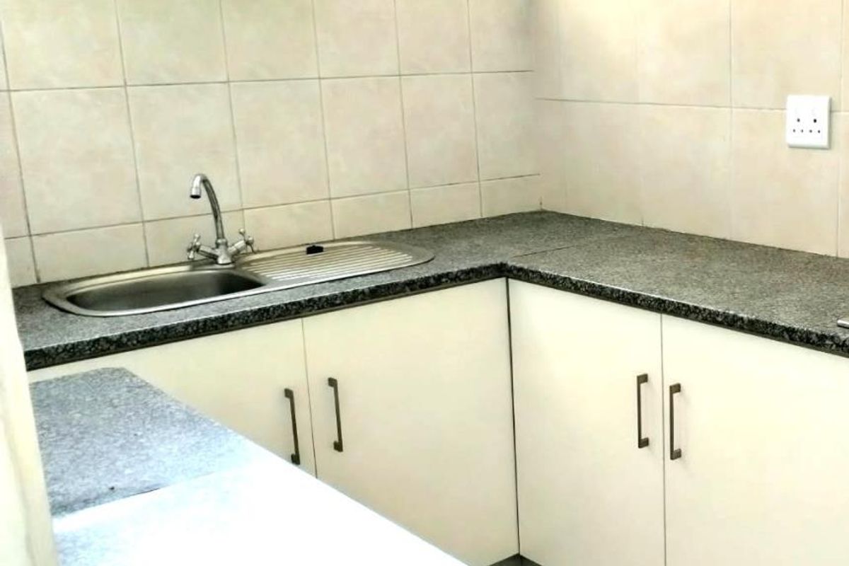 A functional kitchen area featuring white built-in cabinetry, granite-look countertops, a stainless steel sink, and tiled splashbacks.