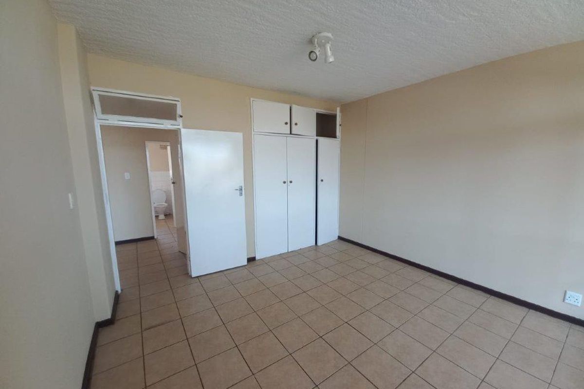 An empty bedroom featuring tiled flooring, built-in cupboards, and direct access to an adjacent bathroom area.