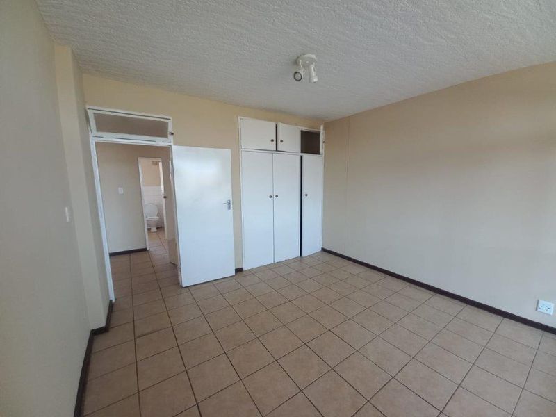 An empty bedroom featuring tiled flooring, built-in cupboards, and direct access to an adjacent bathroom area.