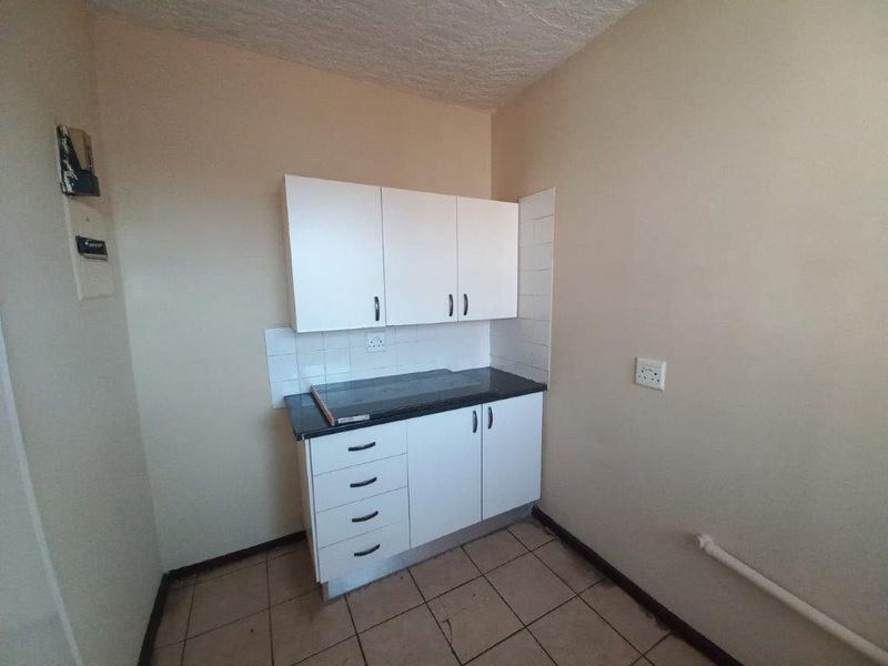 A compact, empty kitchen area featuring basic white built-in cabinetry, a dark laminate countertop, and tiled flooring, ready for a modern update.