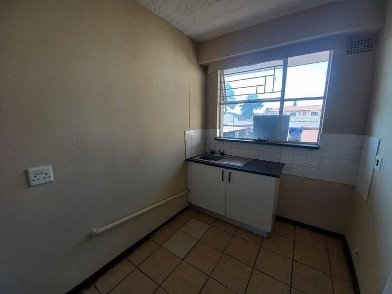 A compact, functional kitchen area featuring basic base cabinetry, a single basin sink, tiled splashback, and tiled flooring.