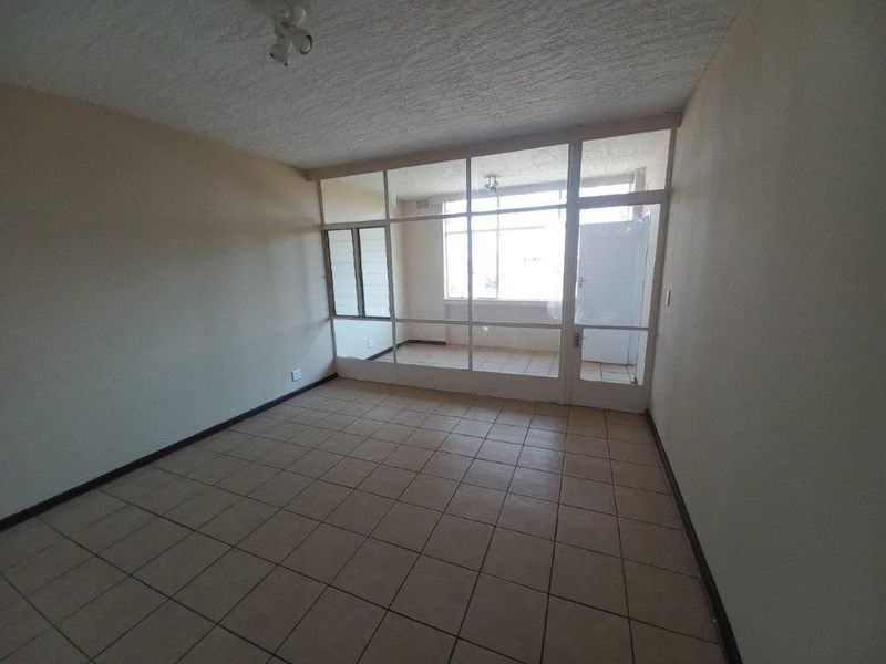An empty living room featuring tiled flooring and a large glass partition wall leading to an enclosed balcony area.