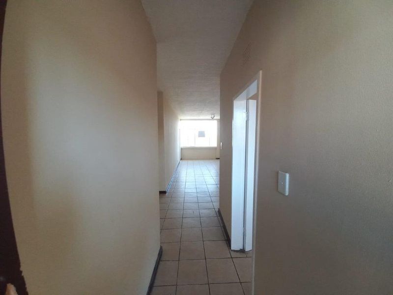 A vacant hallway with neutral walls and tiled flooring, leading towards an open living area with natural light.