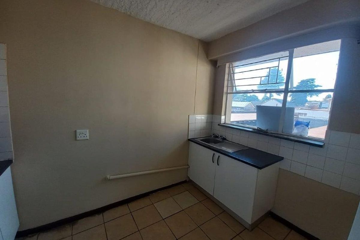 A compact, empty kitchen featuring basic base cabinetry, a single sink, tiled splashbacks, and tiled flooring, offering potential for modernization.
