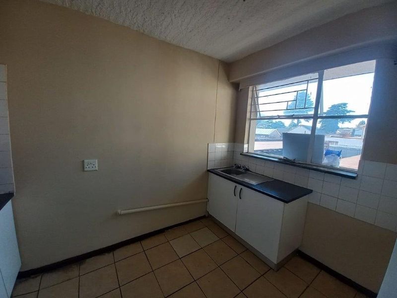A compact, empty kitchen featuring basic base cabinetry, a single sink, tiled splashbacks, and tiled flooring, offering potential for modernization.