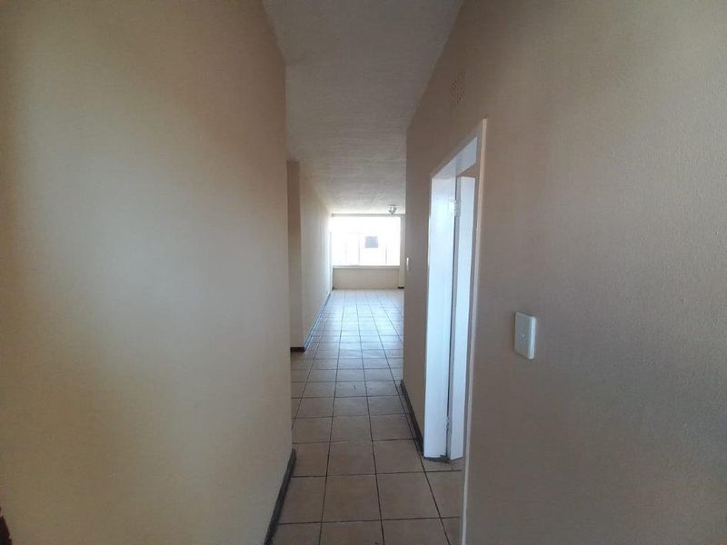 A simple, empty hallway with tiled flooring leading towards a bright living area, featuring neutral wall finishes and standard door frames.