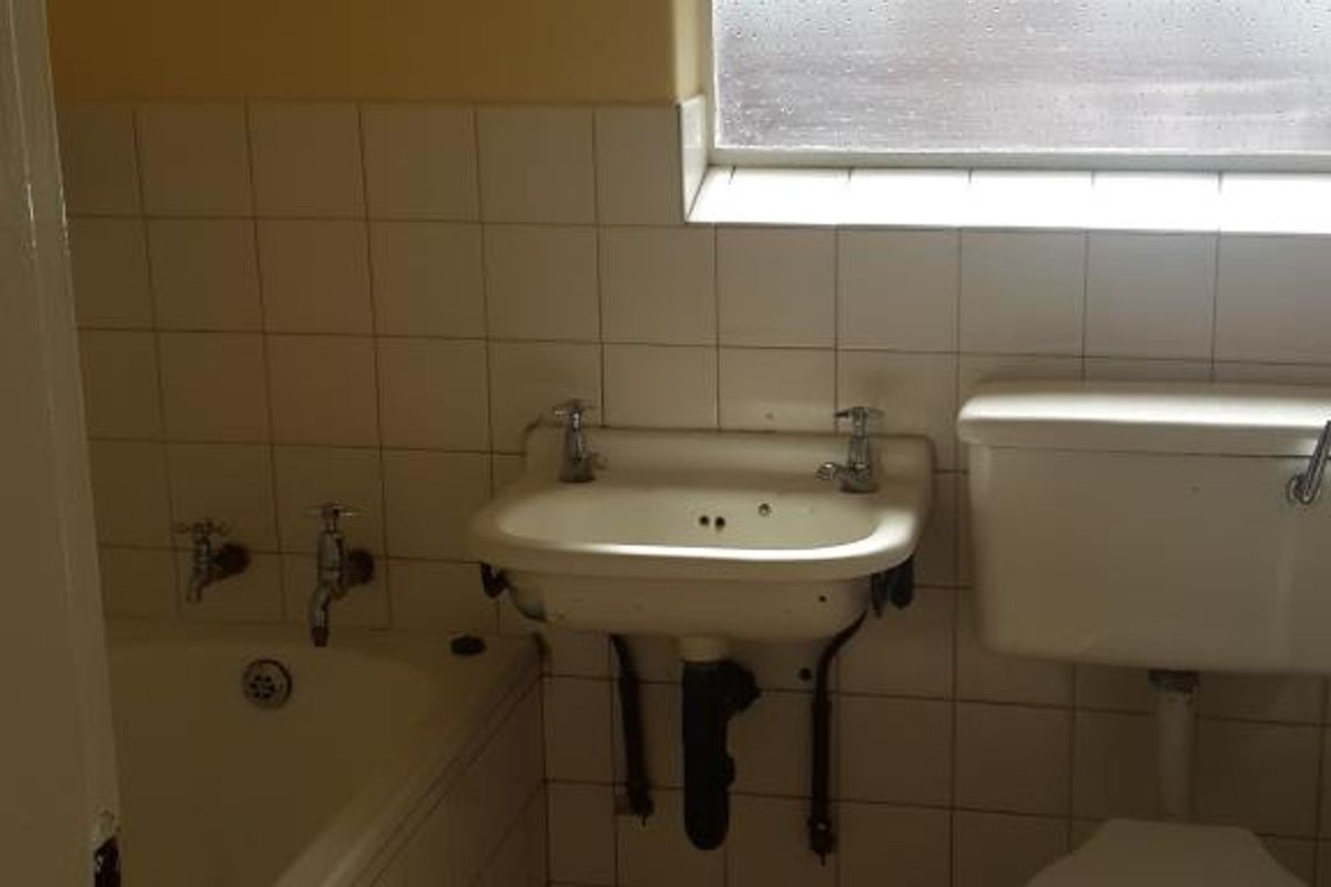 A functional bathroom featuring a bathtub, wall-mounted basin, and toilet with tiled finishes and a window with security bars.