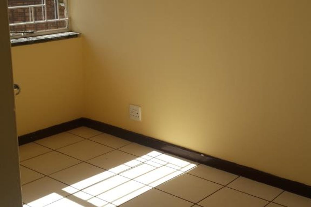 A vacant bedroom featuring tiled flooring, neutral walls, and a window fitted with security bars, offering a clean and simple living space.