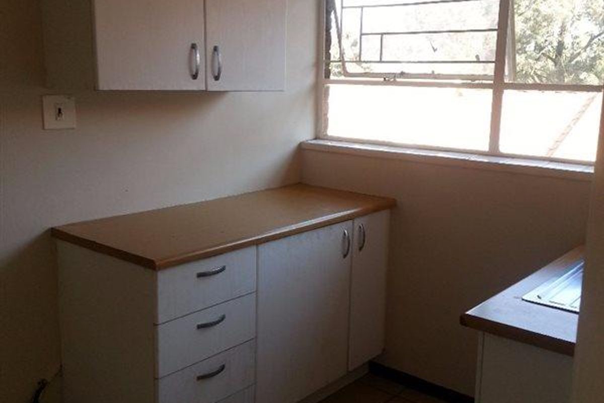 A compact, empty kitchen area featuring built-in cabinetry, laminate countertops, and a stainless steel sink, illuminated by a large window.