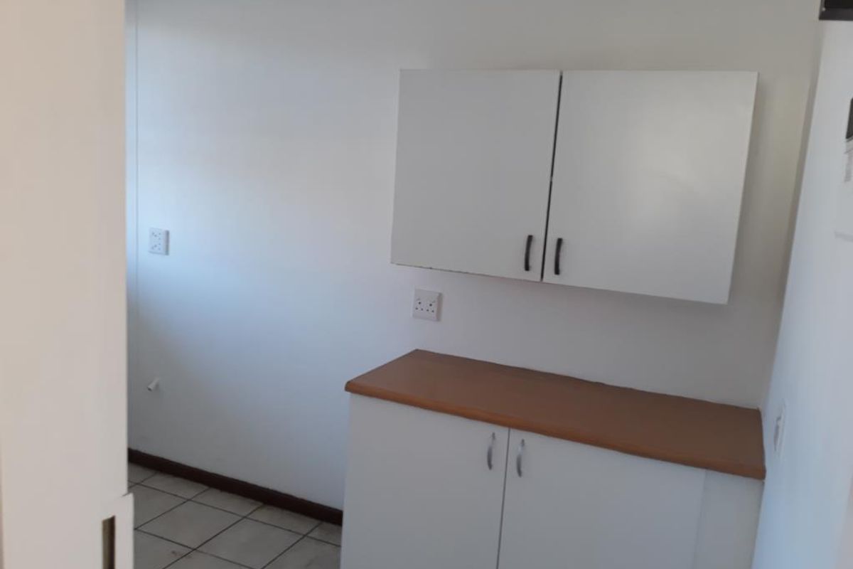 A compact scullery or utility area featuring built-in white cabinetry, a laminate countertop, and tiled flooring, providing functional storage and workspace.