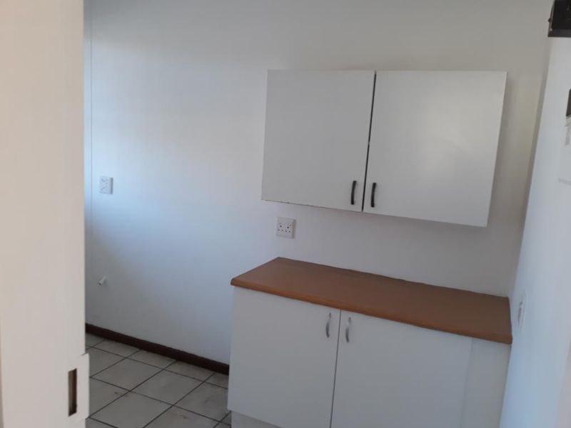 A compact scullery or utility area featuring built-in white cabinetry, a laminate countertop, and tiled flooring, providing functional storage and workspace.