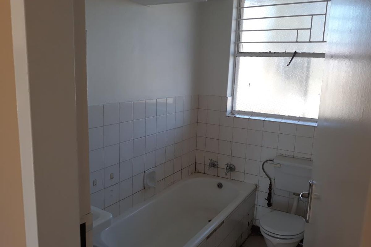 A compact bathroom featuring a standard bathtub, toilet, and tiled wall finishes, requiring cosmetic updates to improve its overall condition.