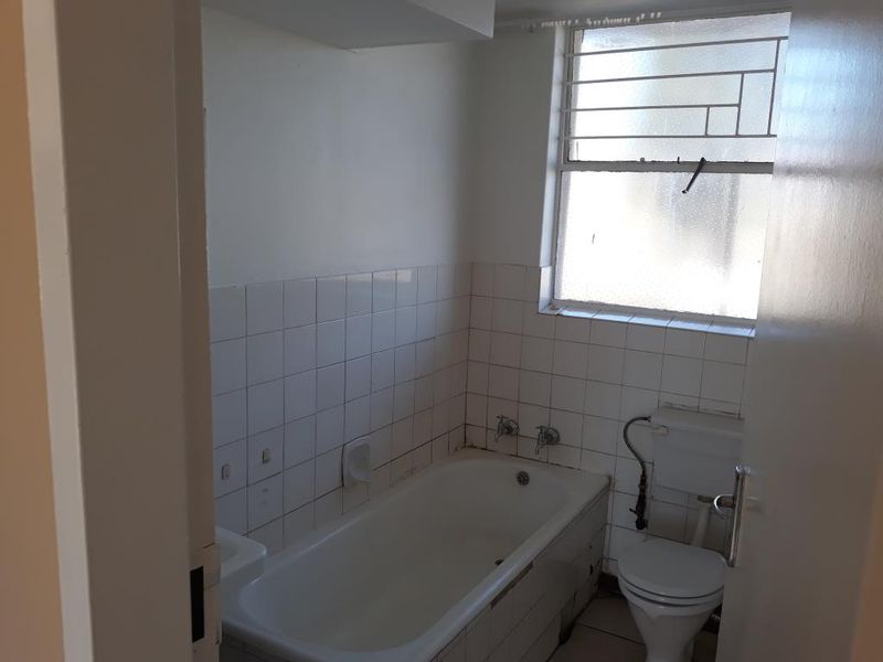 A compact bathroom featuring a standard bathtub, toilet, and tiled wall finishes, requiring cosmetic updates to improve its overall condition.